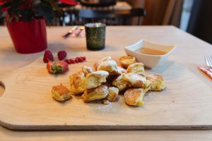 Kaiserschmarrn mit Puderzucker auf einem Holzbrett mit Beeren und Apfelmus.