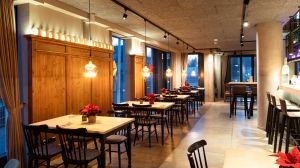 Gemütliche Tischreihen vor einer Holzvertäfelung unter warmem, punktuellem Licht.