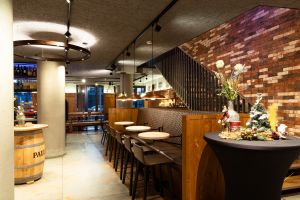 Lederne Sitzbank vor einer Backsteinwand mit kleinen runden Tischen und Treppenaufgang.