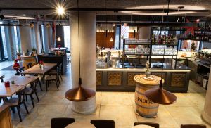 Blick von oben auf den Barbereich mit Weinfässern und kupferfarbenen Hängelampen.