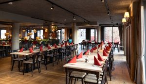 Lange Tafel mit roten Servietten in einem großzügigen, modernen Wirtshausambiente.