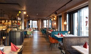 Restaurantbereich mit türkisen und grauen Samtbänken sowie eingedeckten Tischen.