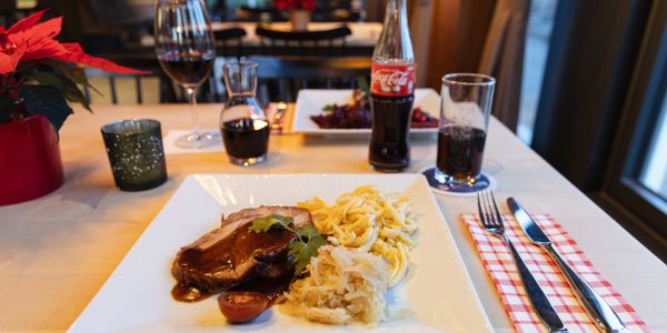 Schweinebraten mit Soße, Spätzle und Sauerkraut neben einer Flasche Cola.