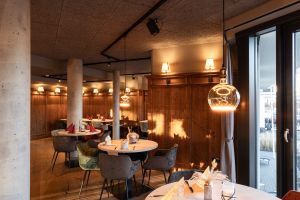 Runde Tische mit bunten Samtstühlen vor einer klassischen dunklen Holzwand.