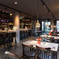 Gastraum mit modernen Pendelleuchten, Bartischen und festlich dekorierten Esstischen.