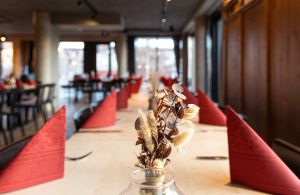 Nahaufnahme eines Trockenblumengestecks auf einem hellen Holztisch mit rotem Farbakzent.