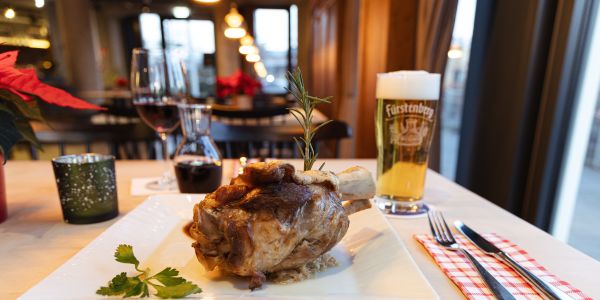 Gebratene Schweinehaxe mit Rosmarinzweig auf Sauerkraut, serviert mit einem Bier.