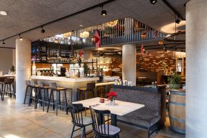 Helle Barlandschaft mit Hochstühlen und Blick in den oberen Gastbereich.